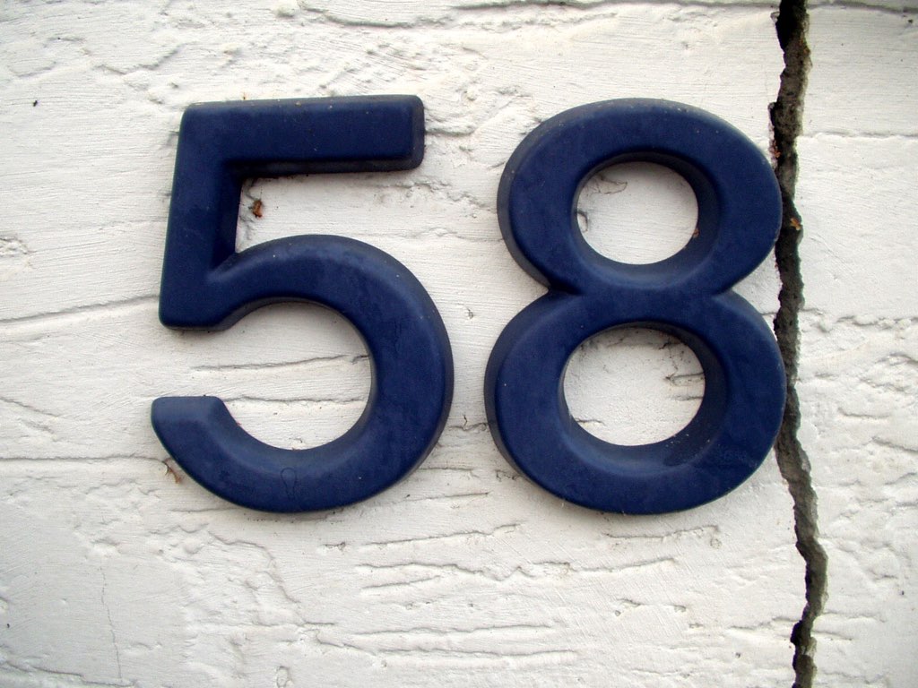 A blue street number on a white stucco background, "58"