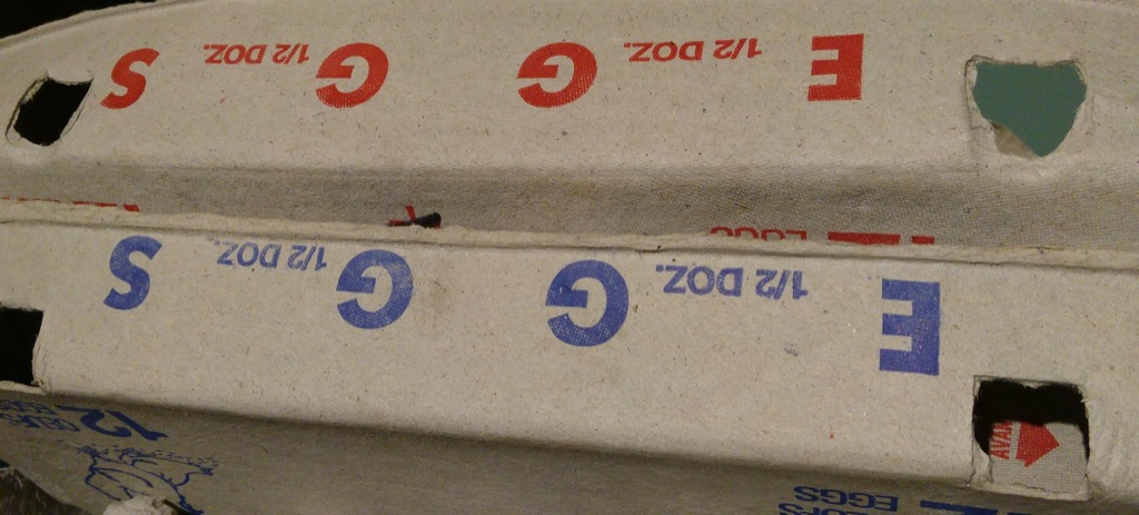 Photo of two egg cartons, one with red printing, one with blue printing, showing the word EGGS, and two 1/2 DOZ., one on either end.