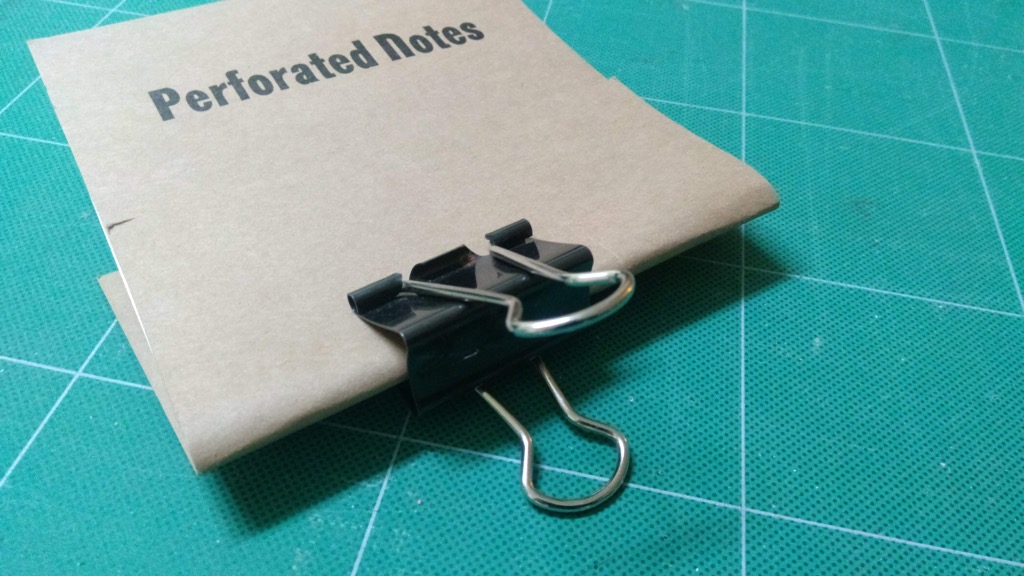 Photo of the binder clamp holding the notebook raw materials together.