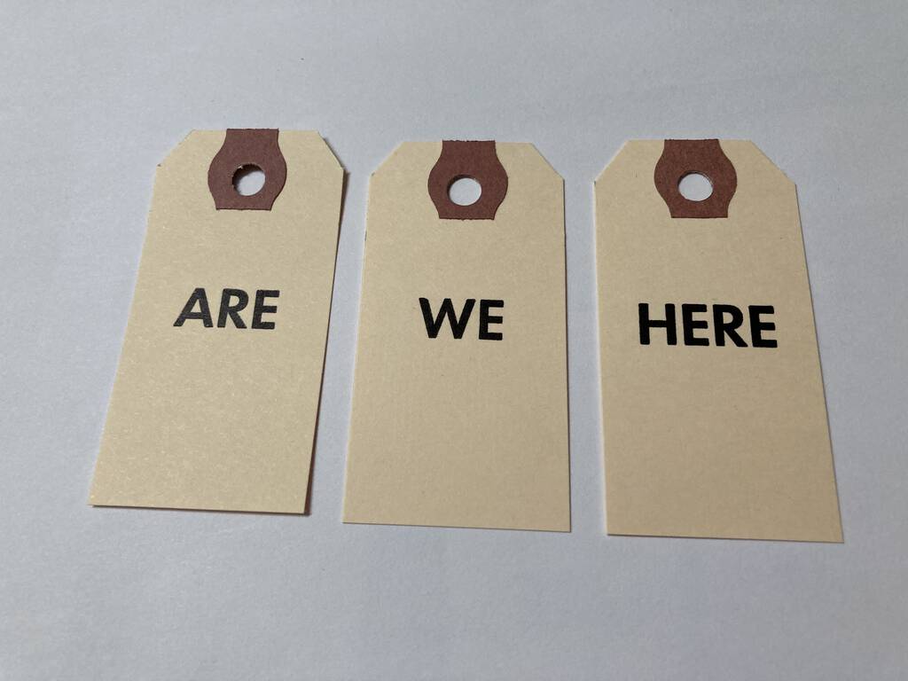 Three tags laid side by side, printed ARE, WE and HERE.