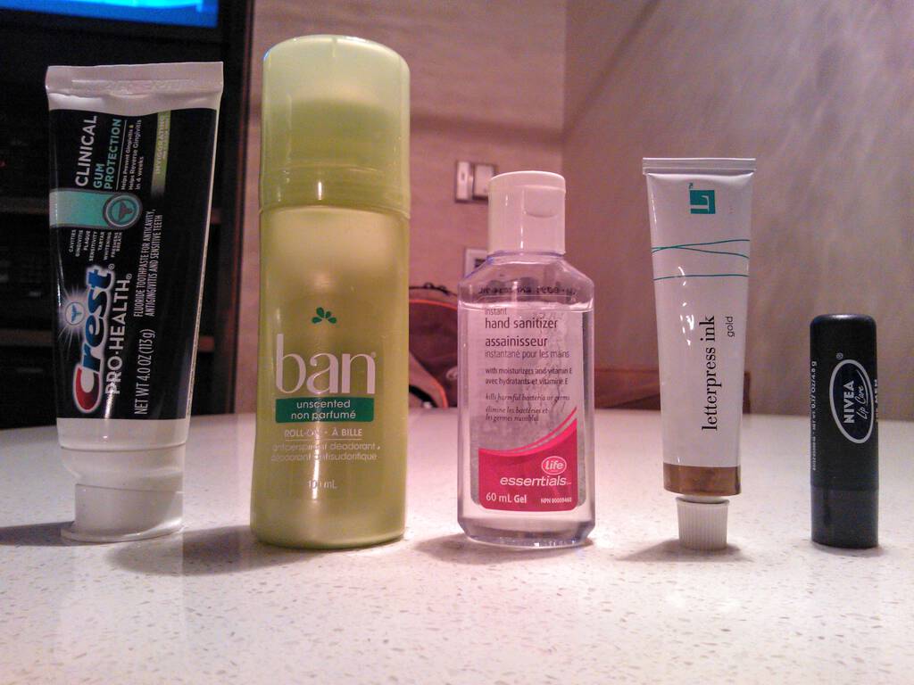 Photo of 5 liquids and gels: toothpaste, deodorant, hand sanitizer, printing ink, lip balm.