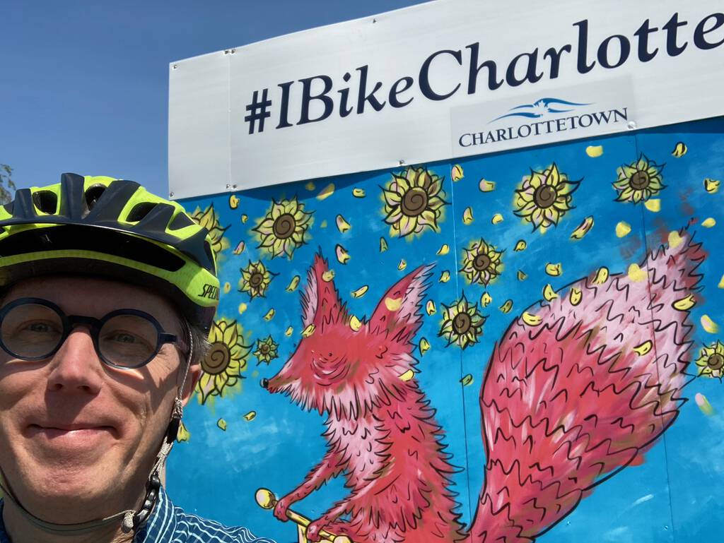 Photo of me, on my bike, in front of the #IBikeCharlottetown billboard on the Confederation Trail near the Farmers' Market