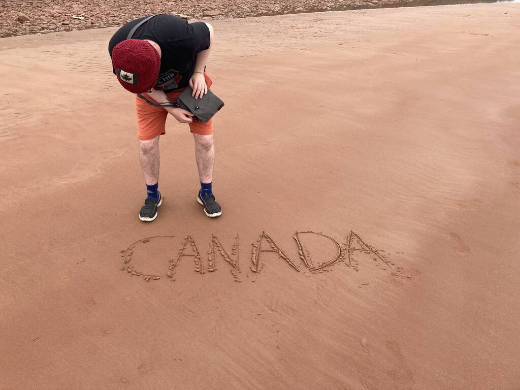 Oliver on the beach, with Canada written in the sand.