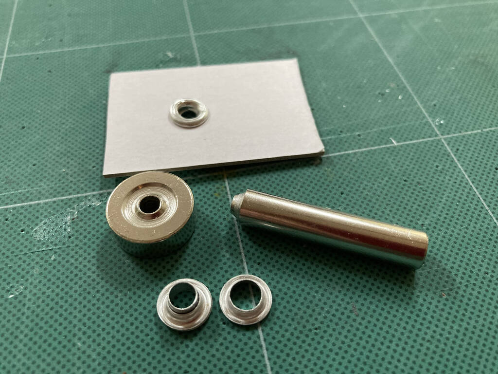 Eyelets and the tools to join them, along with a sample piece of cardboard showing the result.