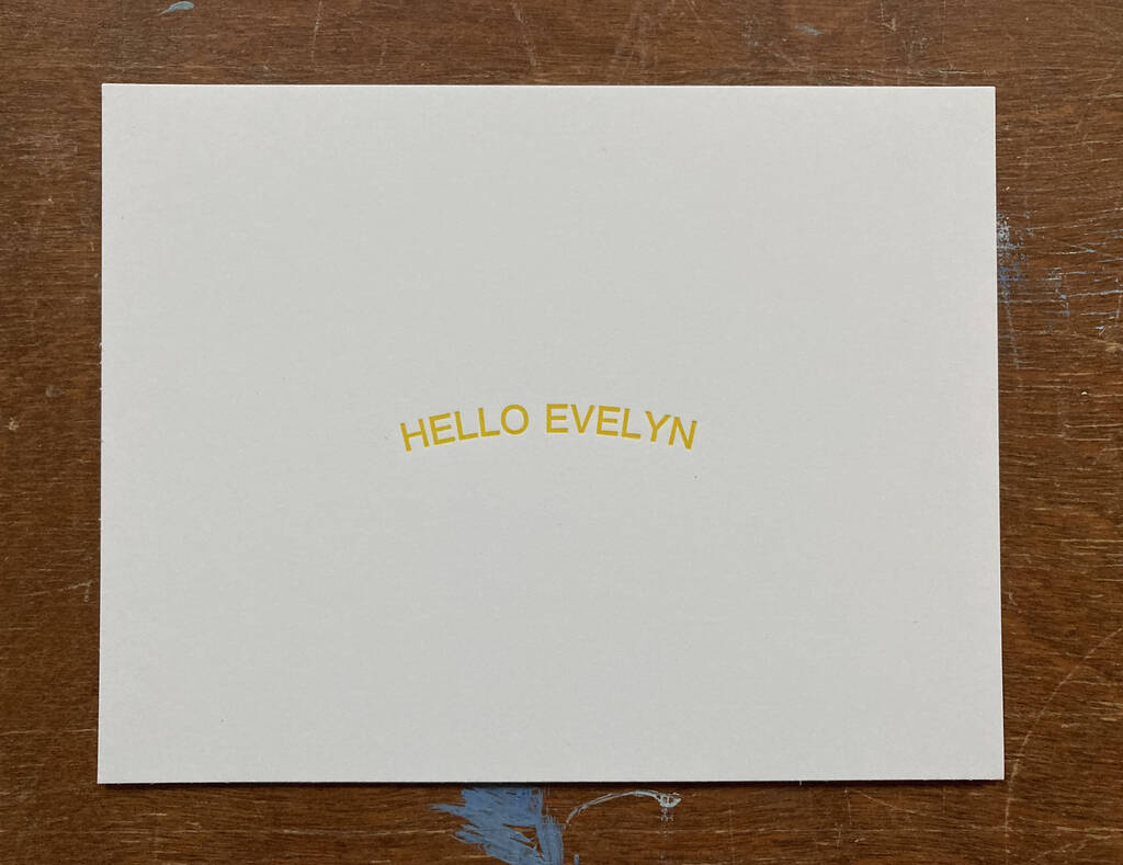 HELLO EVELYN printed in yellow on white card stock, sitting atop a wooden table.