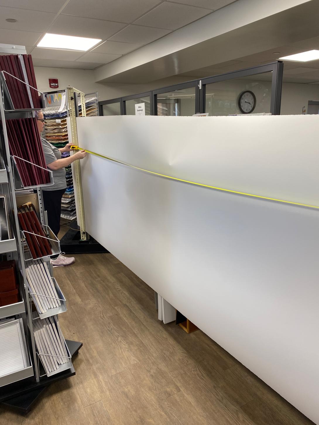 A large roll of paper, about 4 feet tall, being unrolled. There's a woman holding a yellow measuring tape in front of the paper.