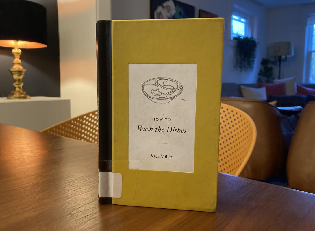 A photo of the Vancouver Public Library copy of Peter Miller's book How to Wash the Dishes: yellow with a black spine, with a sketch of dishes over the title.