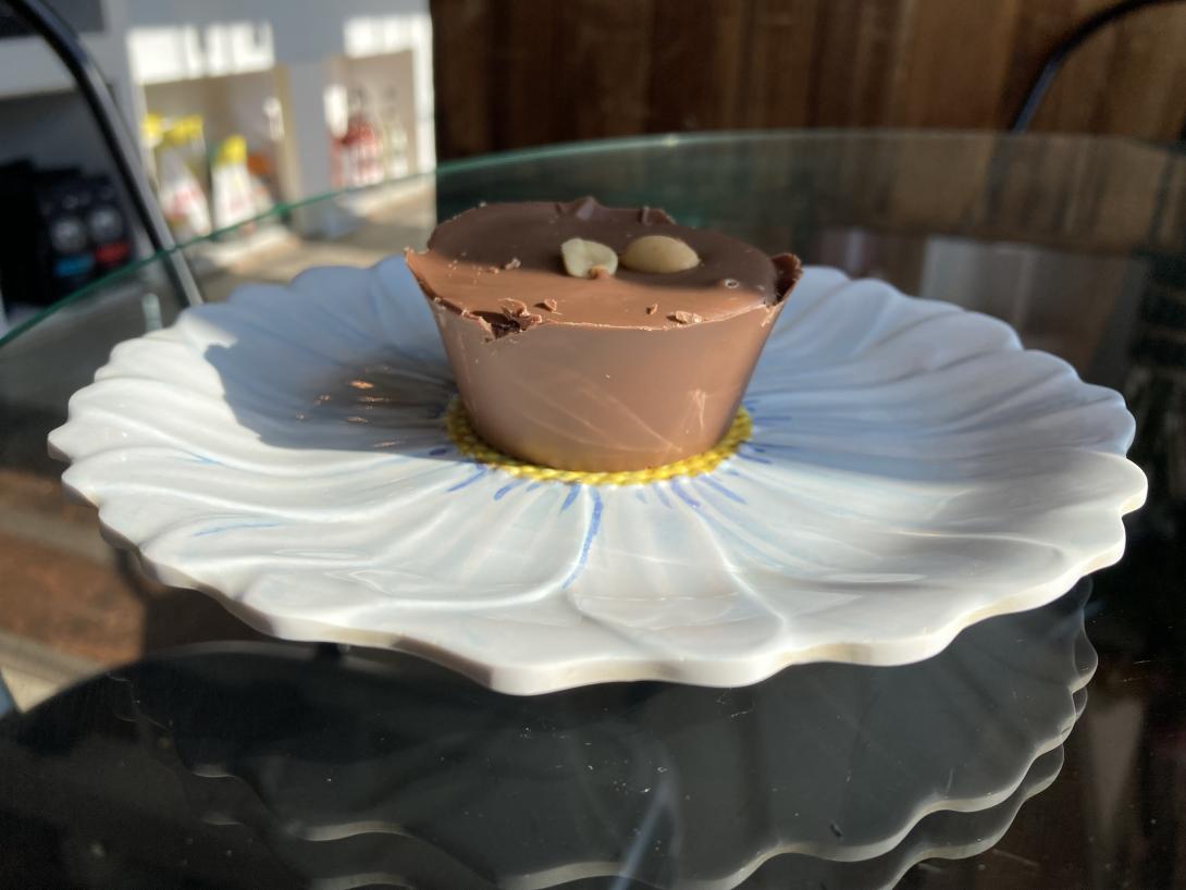 A homemade chocolate peanut butter cup sitting on a sunflower-patterned plate on a glass table, lit by sunshine.