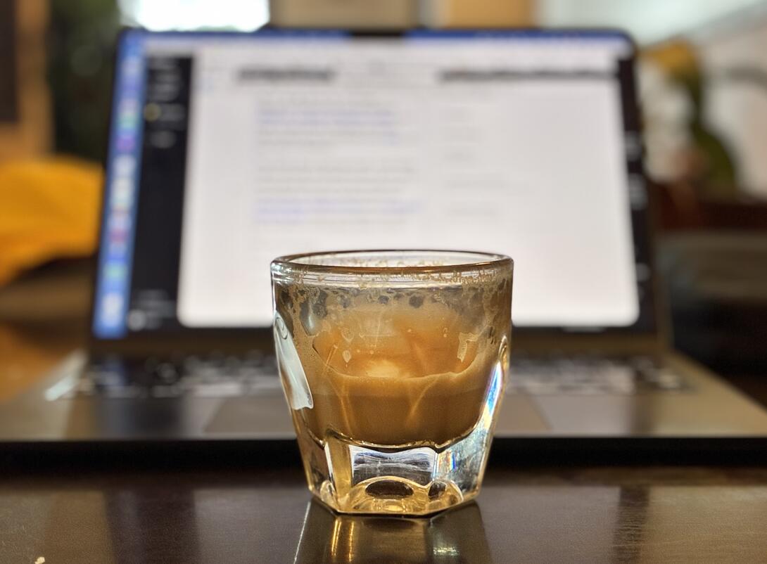 A cortado, ⅔ consumed, in the foreground against a blurry background of a MacBook Air.