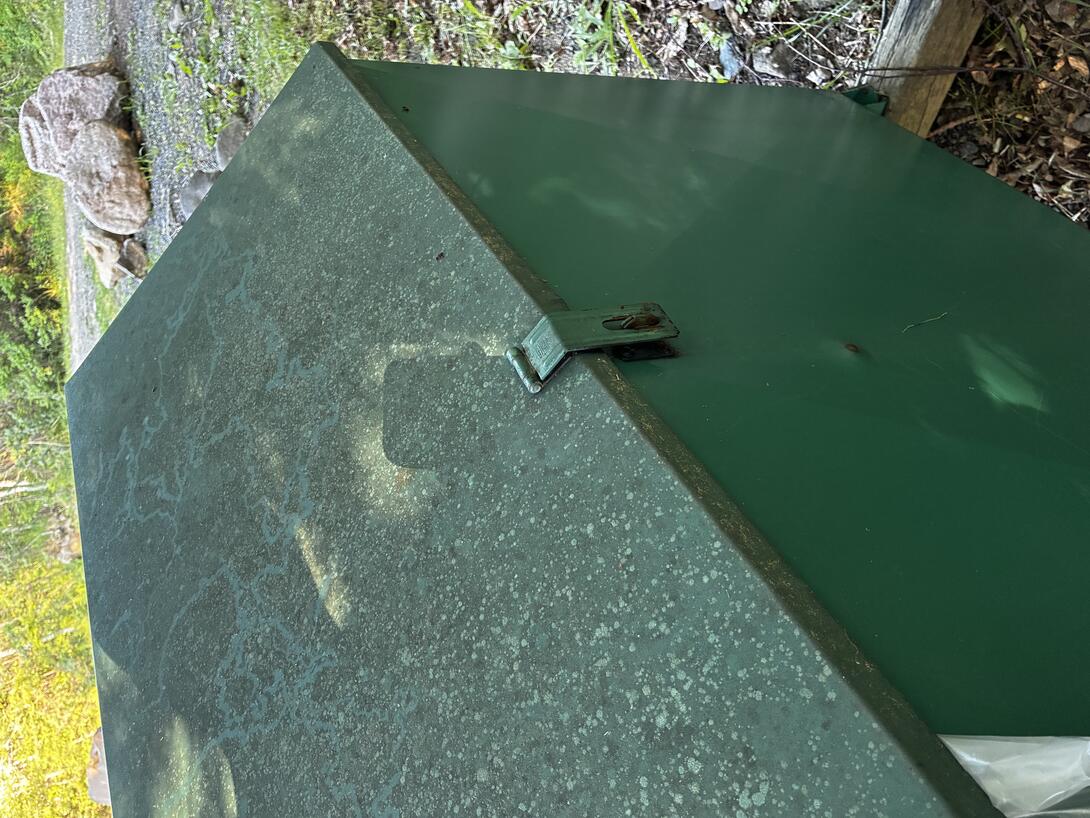 The back of an unlocked green metal garbage bin.
