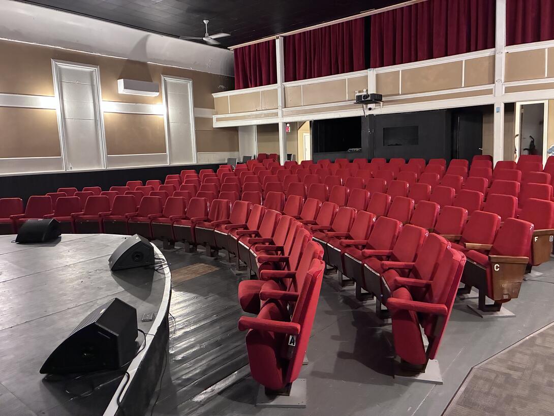 A view inside Souris Show Hall, with red chairs and a balcony in the distance.