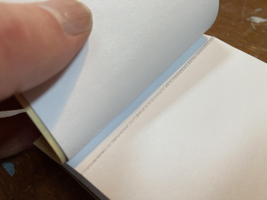 My thumb holding open the notebook, showing the perforations.