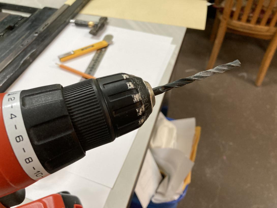 My cordless electric drill, with a 5/64 inch drill bit installed, against the background of some printing tools.