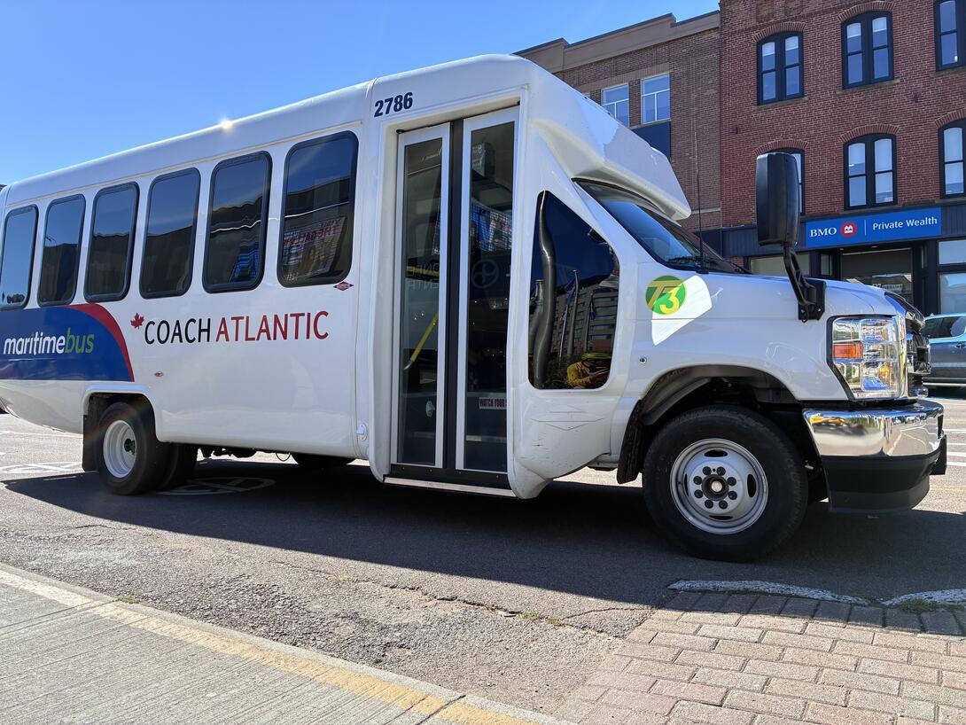 Photo of a small bus waiting at the stop on Queen Street. It’s white and blue with Coach Atlantic and T3 branding.