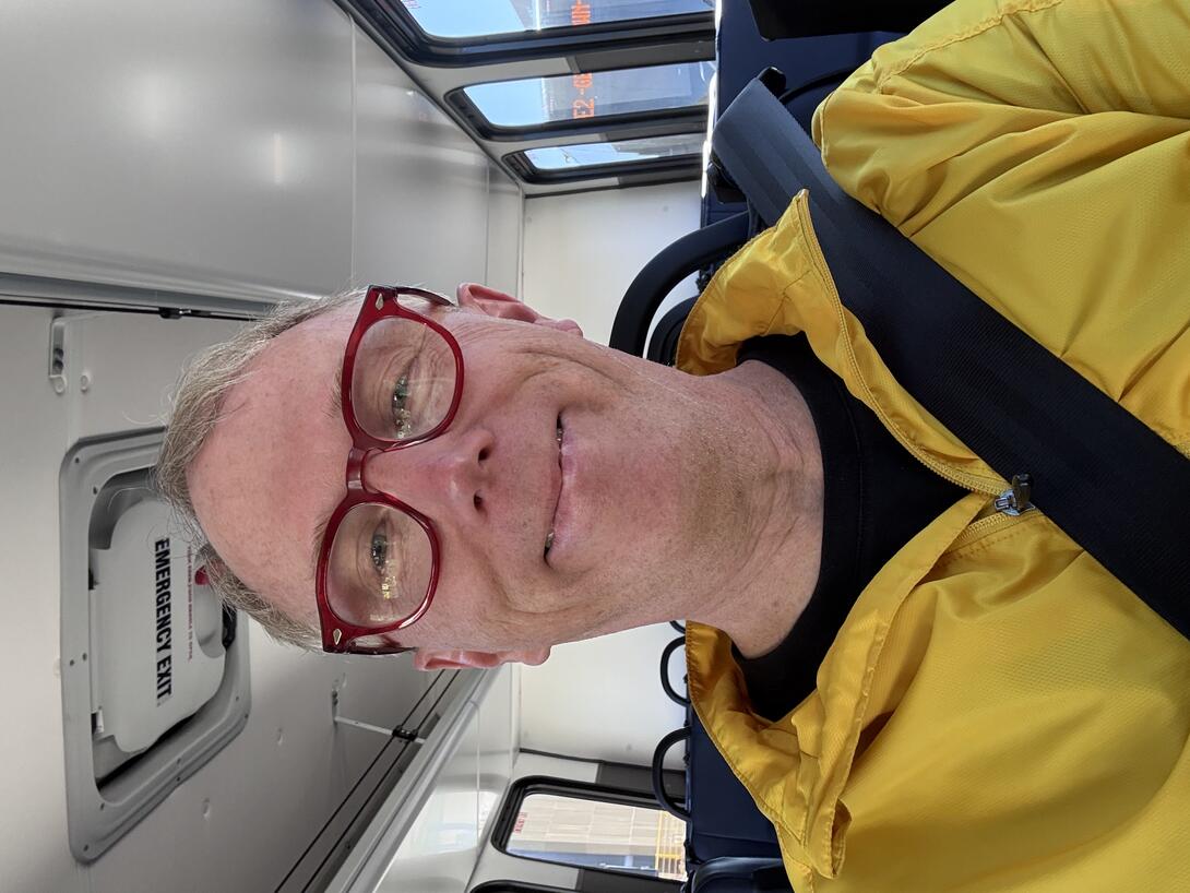 Me, in a yellow jacket, wearing a seat belt, smiling, on the bus.