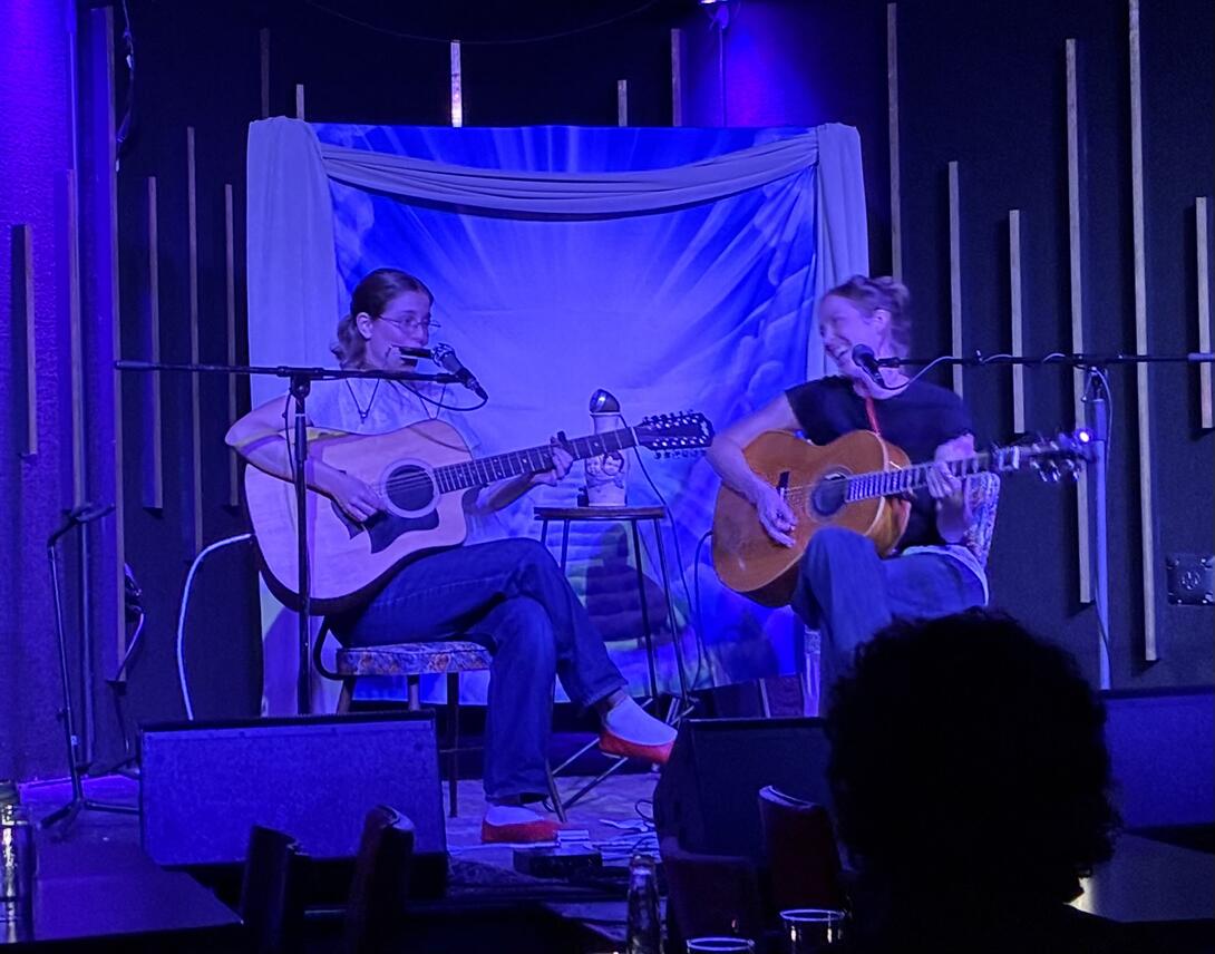 True Mountain Laurel, on stage at Trailside: against a backdrop of a blue "stairway to heaven" blanket, two women playing guitars.