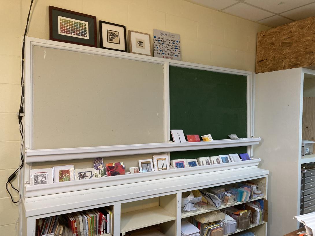 A bulletin board and a black board. On top of them are 4 pieces of art, framed.