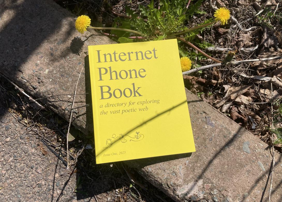 A bright yellow book, with “Internet Phone Book” printed on the cover. The book is sitting on a piece of concrete, with three bright yellow dandelions, extending from underneath it