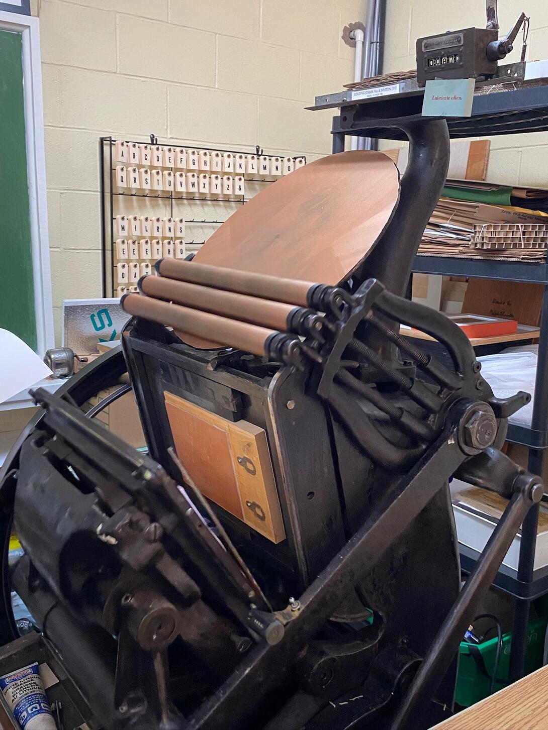 Lino block mounted on platen press, printing in copper colour.