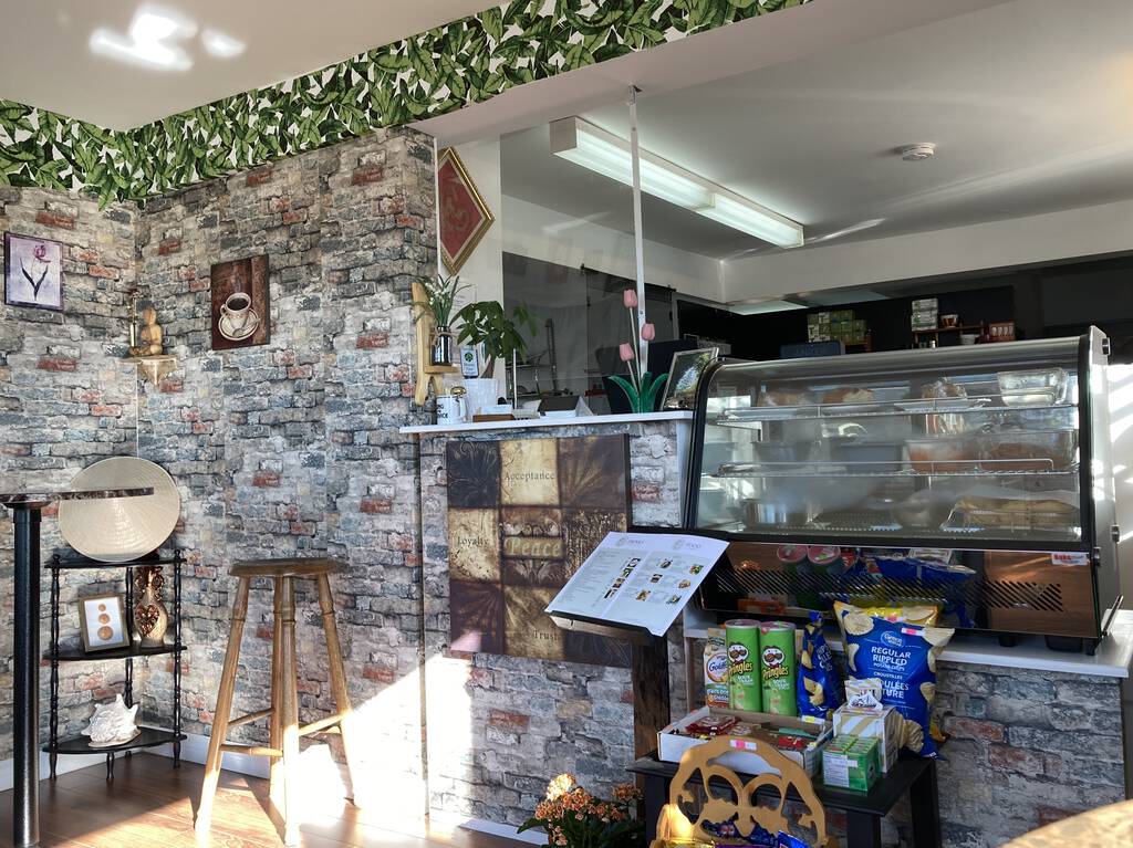 Inside the restaurant, showing cash area, refrigerated case, and decor, which features faux grey brick wallpaper trimmed with faux green leaf border.