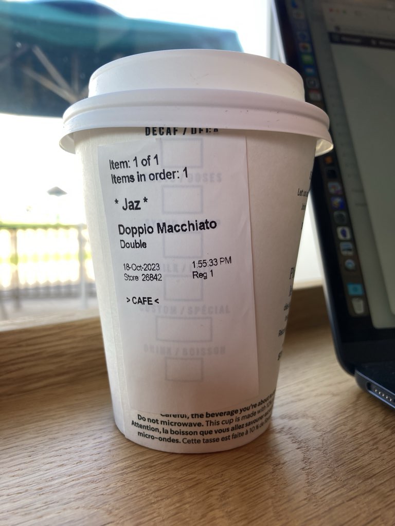 A small coffee cup with Starbucks sticky label affixed, with the name Jaz printed on it, and a Doppio Macchiato label