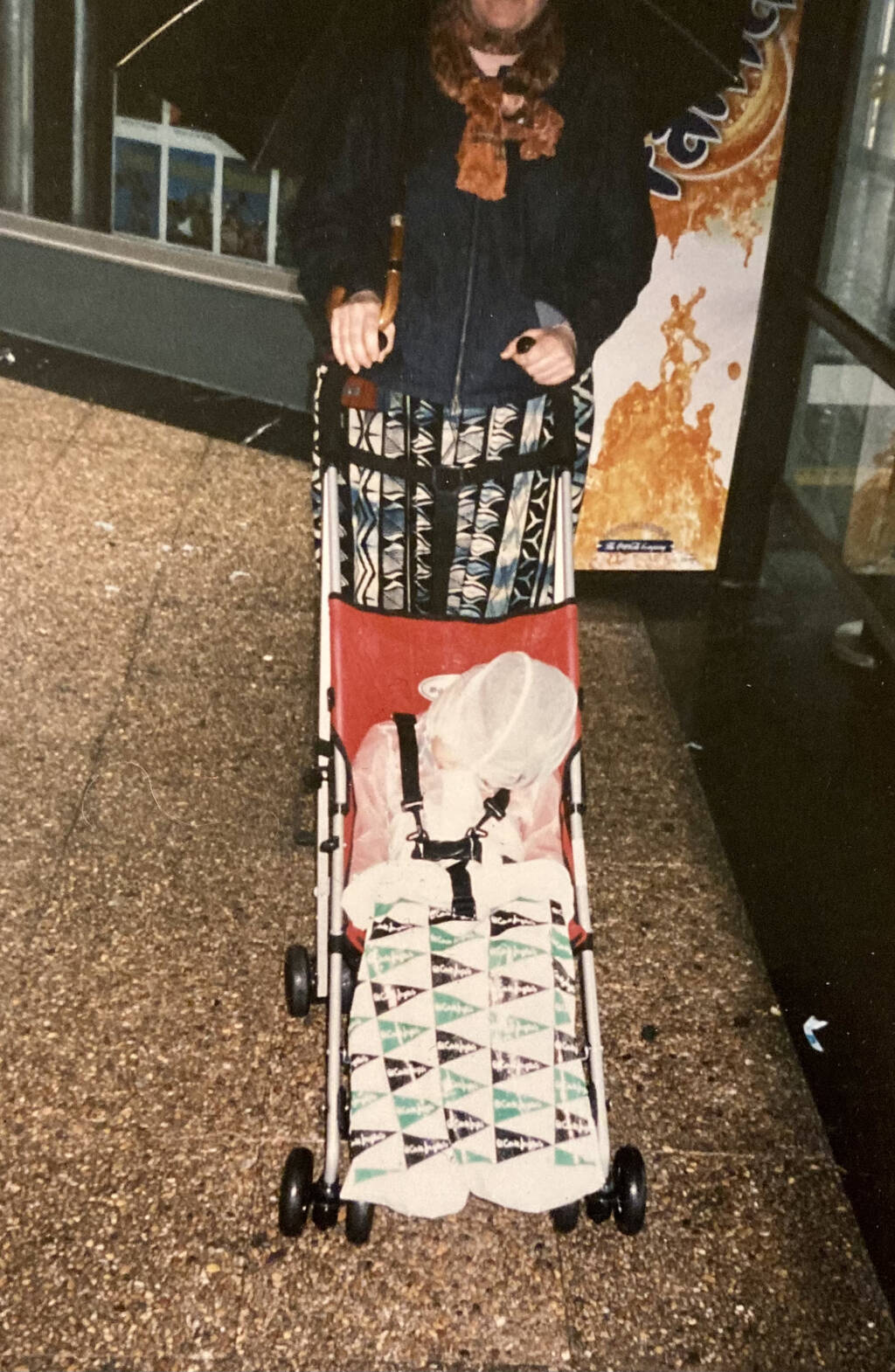 Photo of Oliver in an umbrella stroller with a shopping bag on his feet.