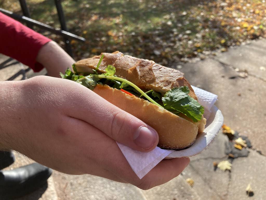 Oliver holding a sandwich from Non La in his hand: a baguette filled with vegetables and herbs.