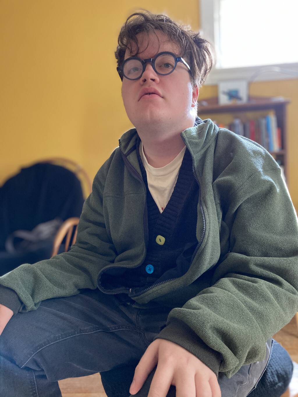 Photo of Oliver sitting in the living room, dressed as Peter, in a cardigan, and wearing my round, blue eyeglasses.