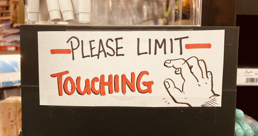"Please Limit Touching" hand-lettered sign in The Bookmark, with a cartoon-like drawing of a reaching hand beside,