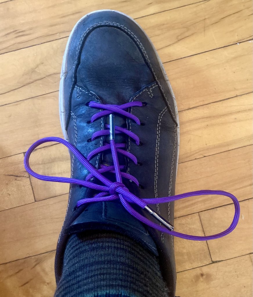 Purple shoelaces on black shoes, on a hardwood floor background.