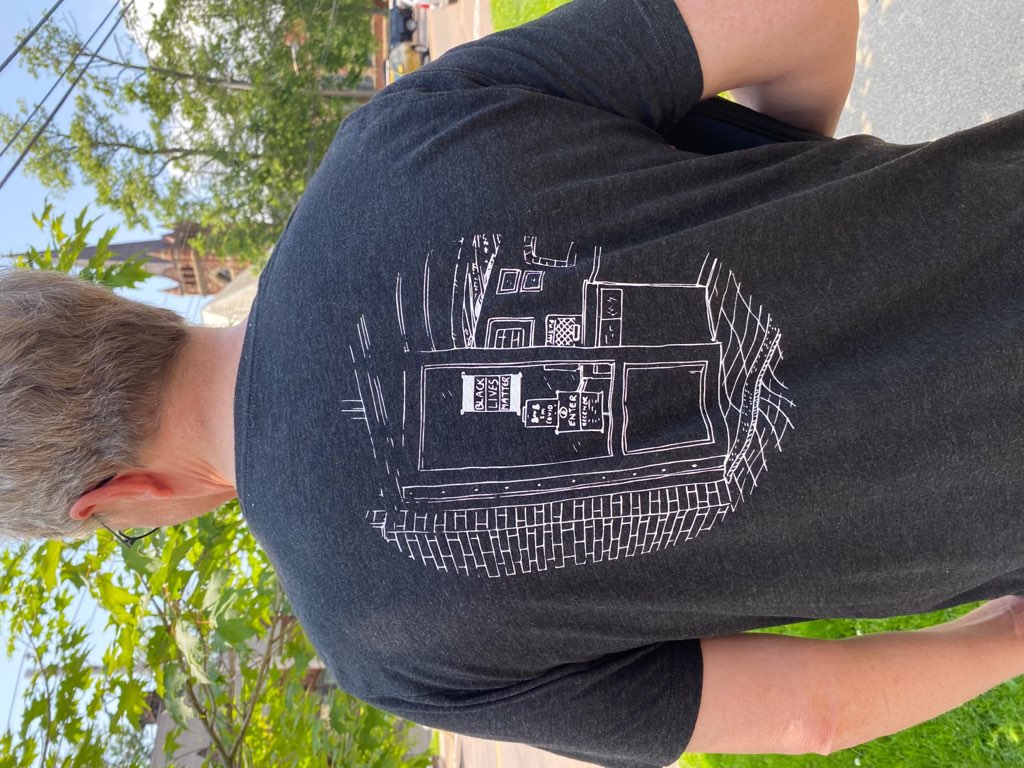 Photo of me, from the back, wearing a Receiver Coffee staff shirt that features my black and white sketch of the patio at Victoria Row
