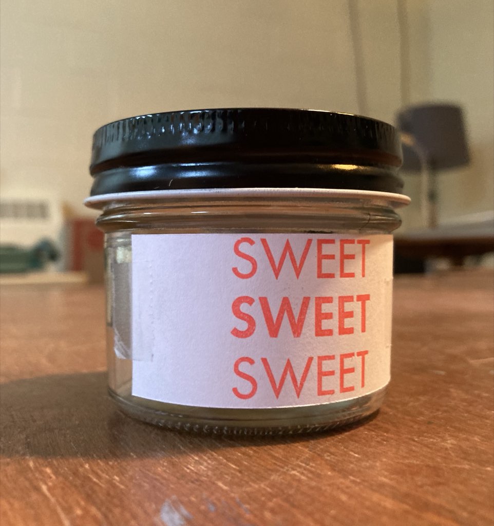 The words SWEET SWEET SWEET, printed in red, on white paper, stuck on a small jar.