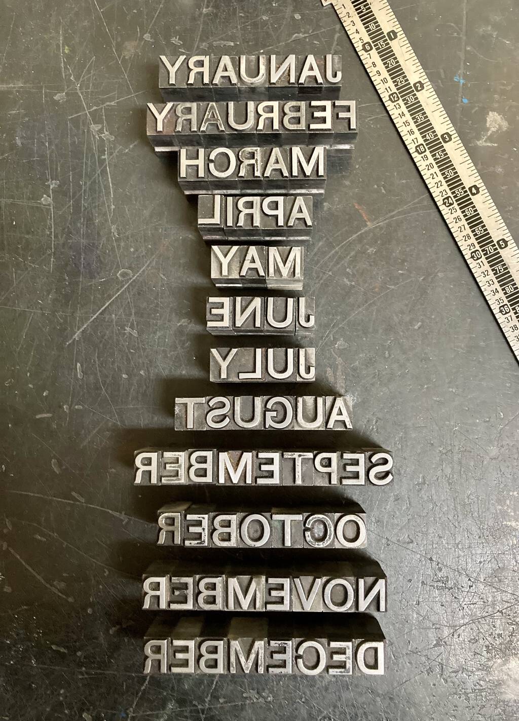 The names of all the months, in metal type, set right to left, on a metal table.