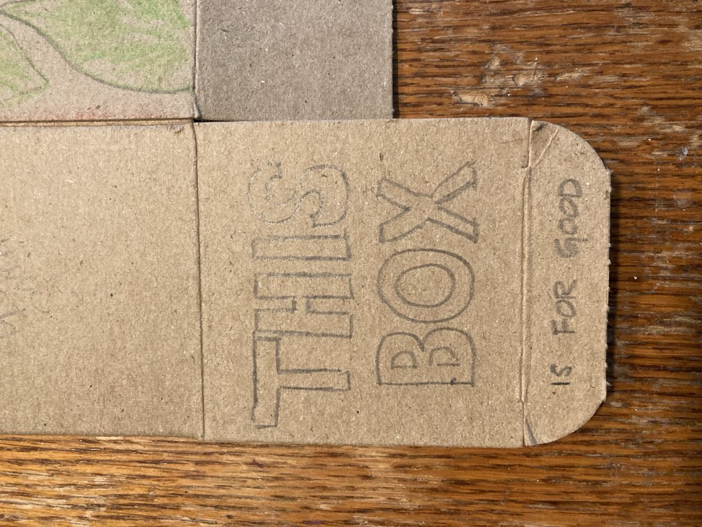 "This box is" written in pencil on a cardboard box lid.