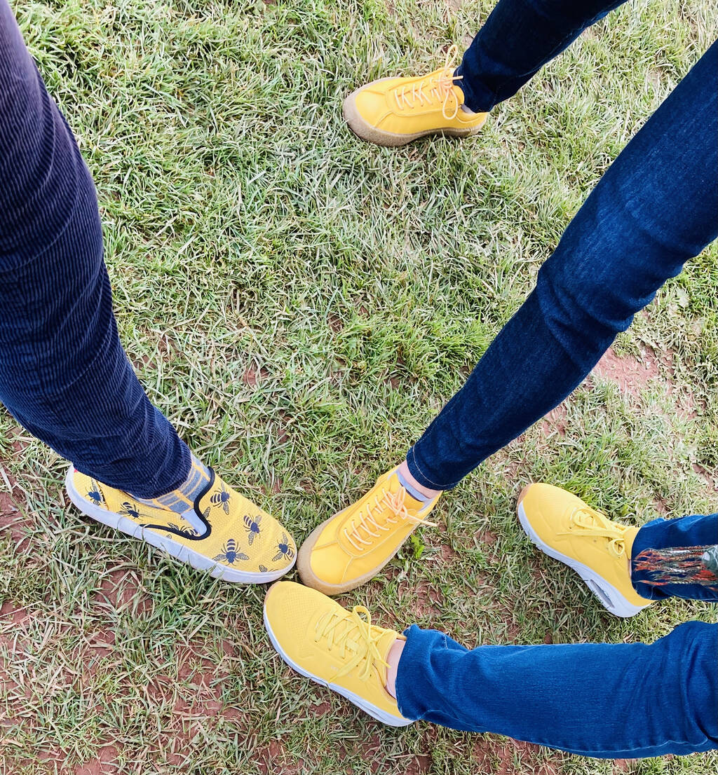Three pairs of Yellow Shoes on green grass, attached to their owners' feet.